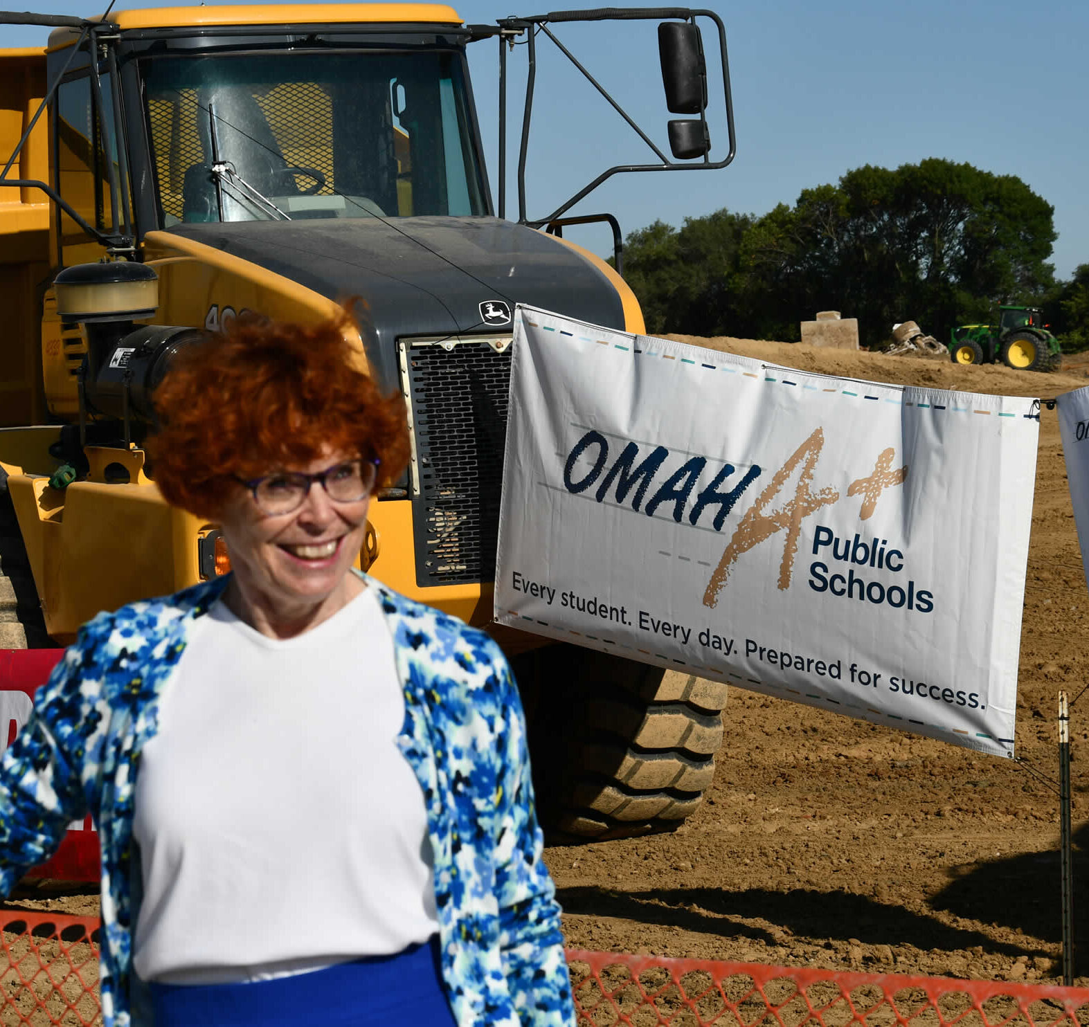 Jane standing in front of a banner that says Omaha A+ Public Schools and a construction machine.